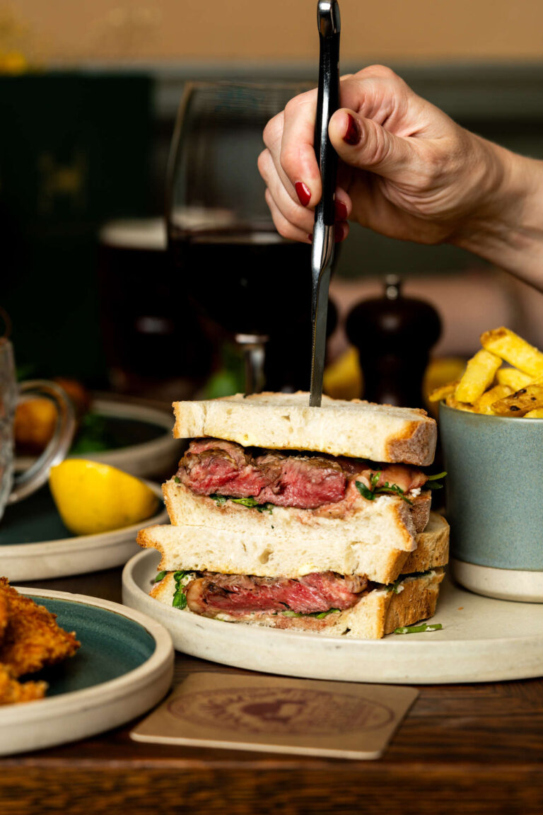 Pink Steak Sandwich on white bread with a knife stuck in
